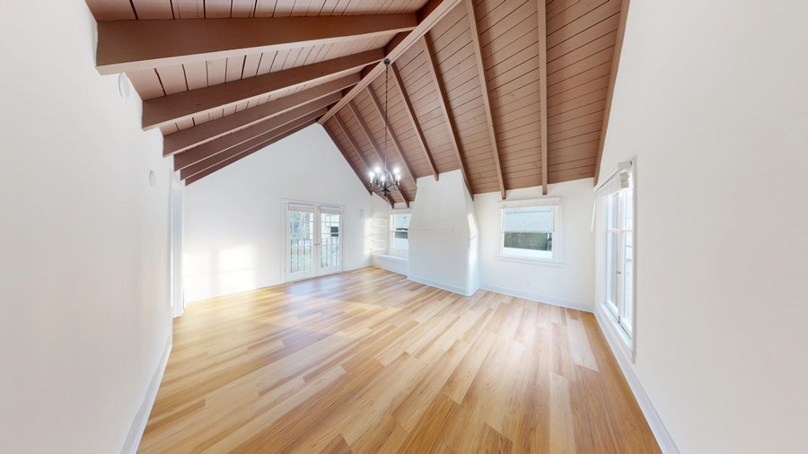 A room with wooden floors and a sloped ceiling with windows on the side.